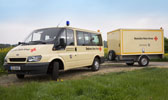 Foto: Ein Einsatzwagen mit Anhänger vor einem blühenden Rapsfeld.